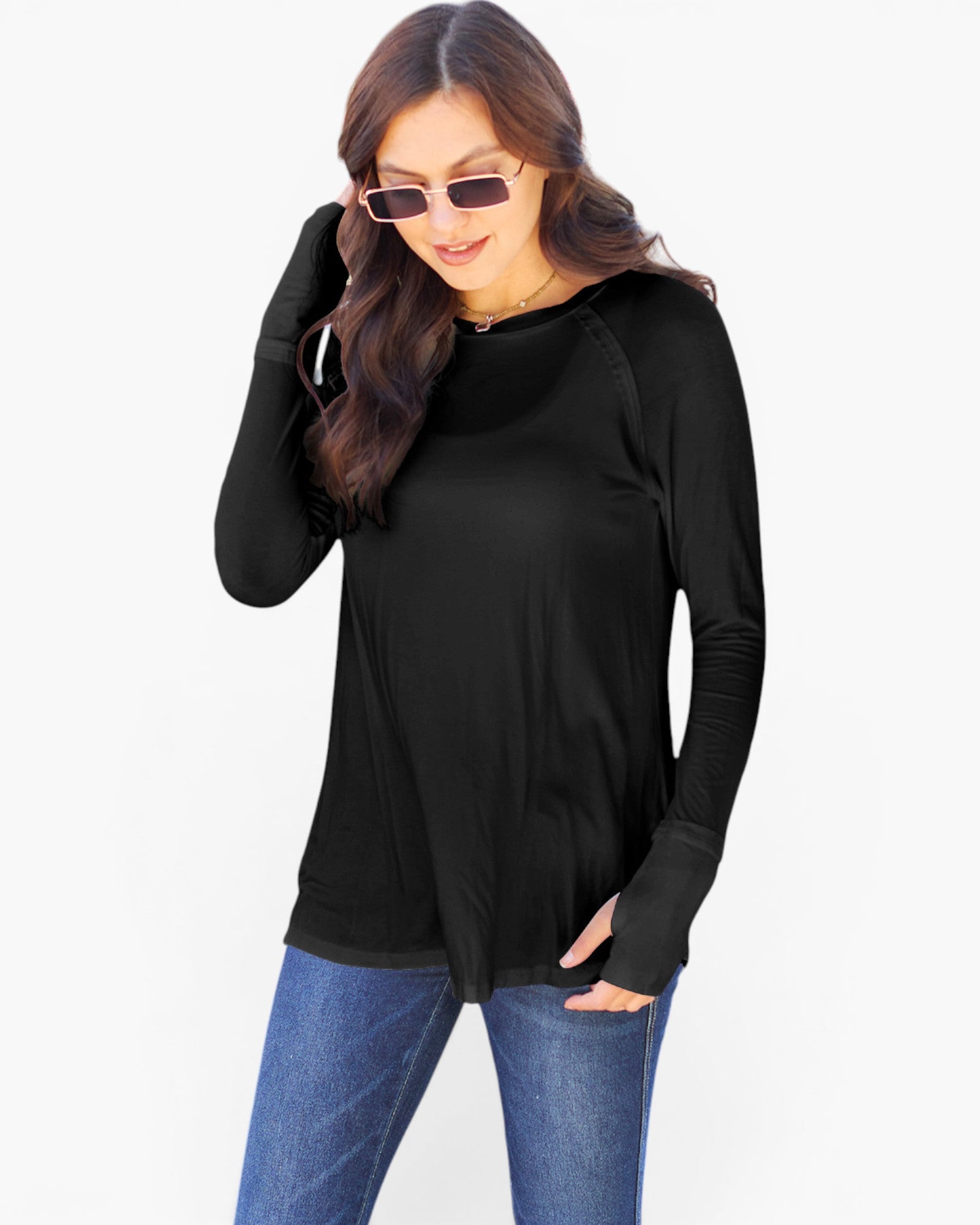 A woman wearing a black long-sleeve top with a relaxed fit, raglan sleeves, and a small V-neckline, paired with blue jeans against a plain white background.