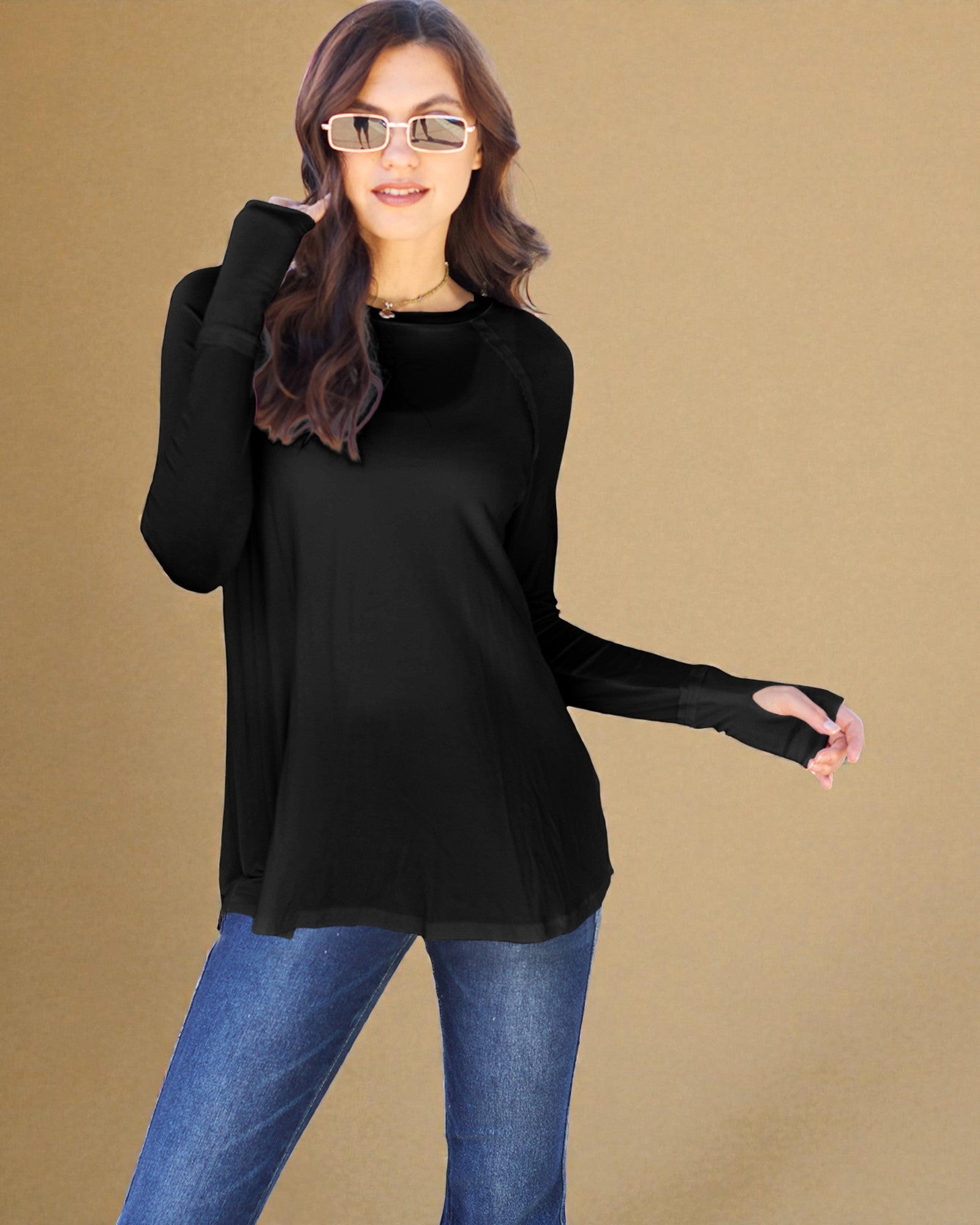 Woman wearing a black long-sleeve top and blue jeans against a beige background