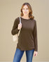 Woman wearing a brown long-sleeve top and blue jeans, holding a beige handbag against a beige background.