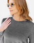 A woman wearing a dark heather gray long-sleeve crewneck top, styled with gold-framed sunglasses, shown in a close-up profile shot against a plain white background.