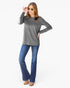 A woman modeling a heather gray long-sleeve top with blue flare jeans and brown shoes, standing against a plain white studio background.