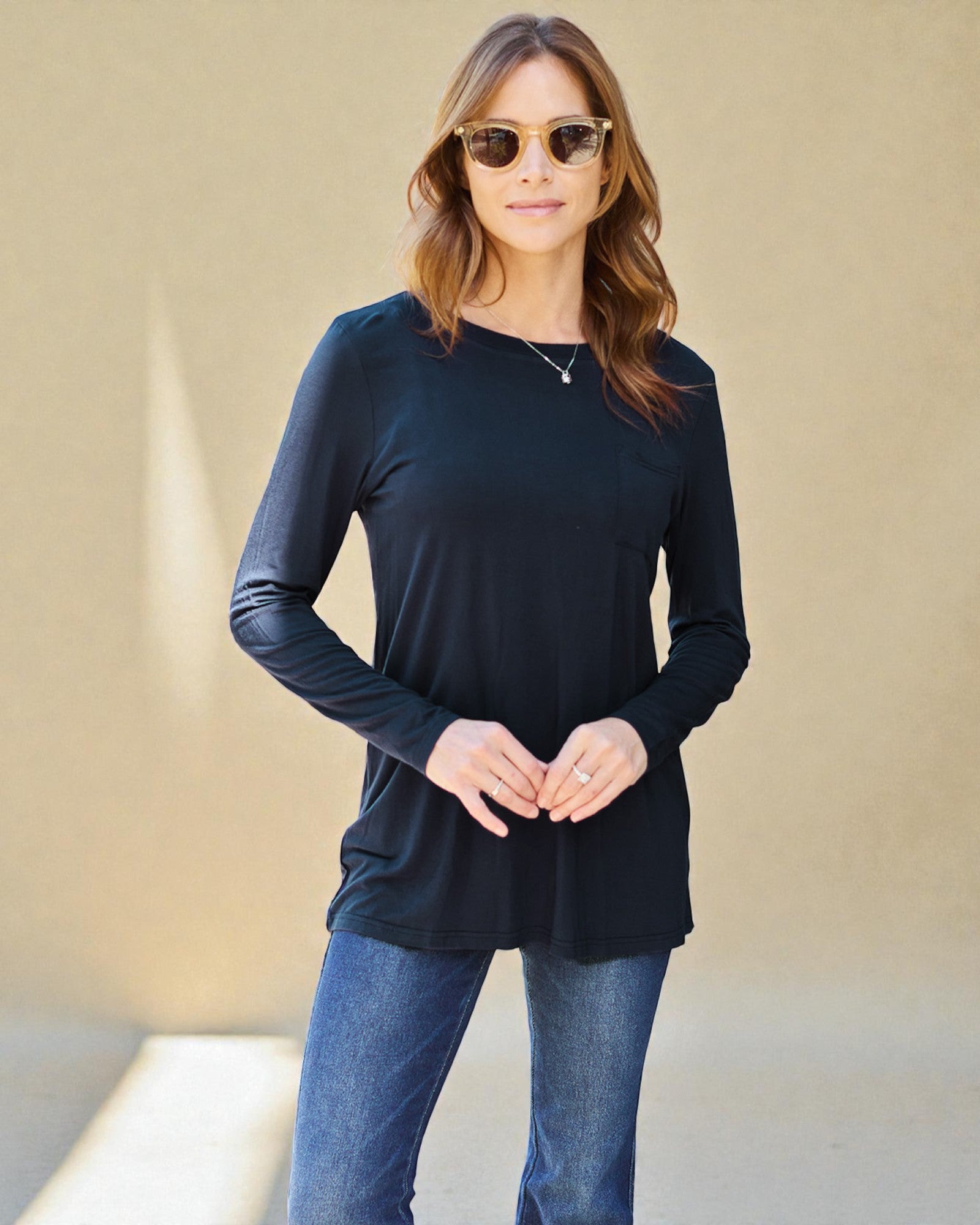 Woman wearing a black long-sleeve top and blue jeans against a beige background