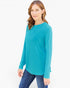 A woman modeling a bright turquoise long-sleeve top with blue jeans against a plain white studio background.