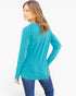 A woman wearing a bright turquoise long-sleeve top and blue jeans, shown from a three-quarters back view against a plain white studio background.