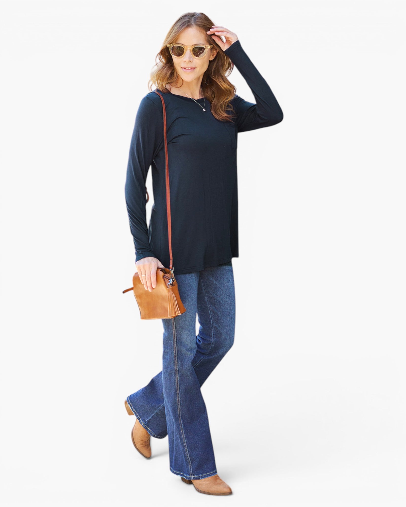 A woman modeling a black long-sleeve top with blue flared jeans, wearing sunglasses and carrying a small tan crossbody bag, set against a plain white studio background.