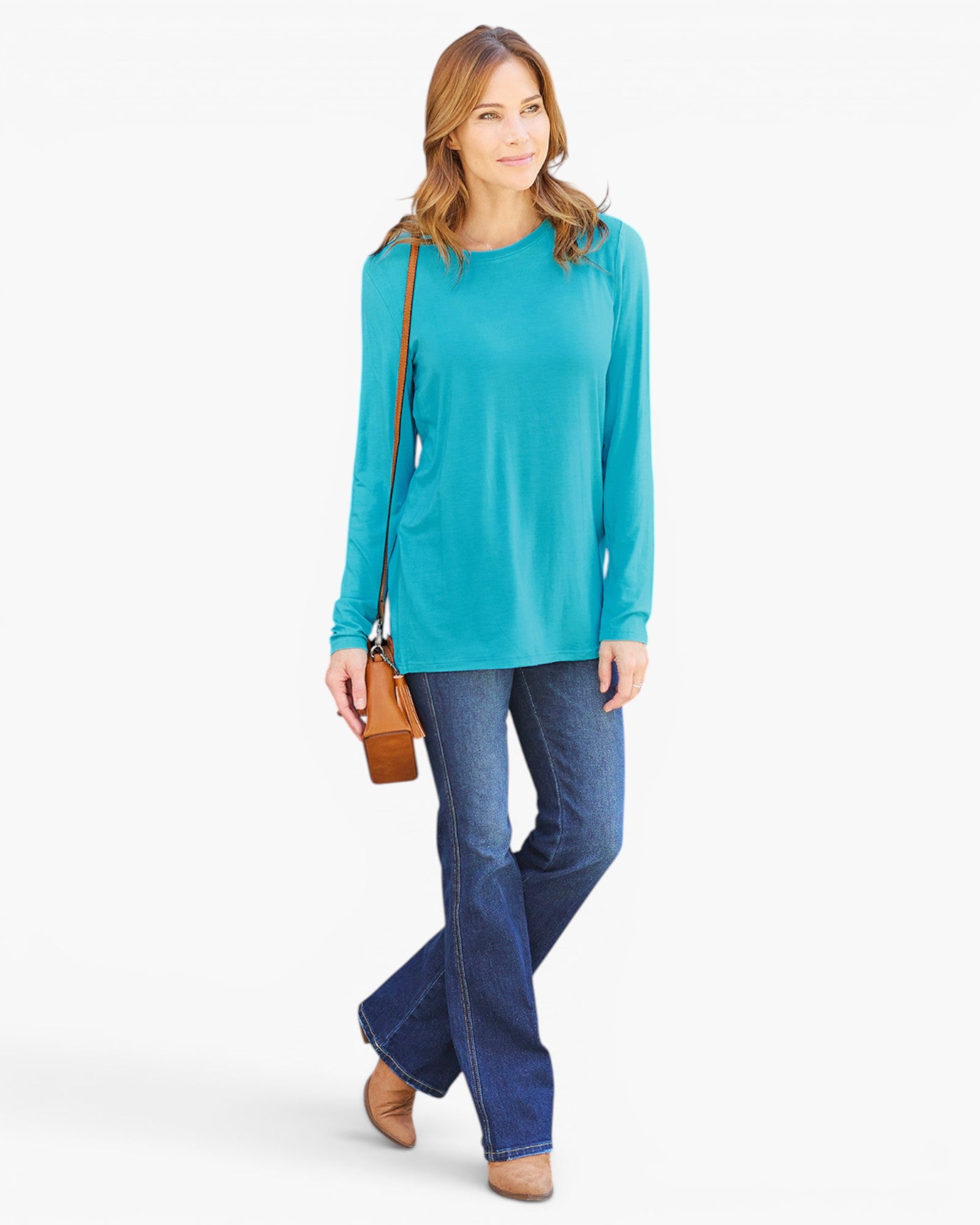 A woman modeling a turquoise long-sleeve crewneck top with blue jeans and a small brown crossbody bag, photographed against a clean white studio background.