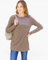 A woman modeling a long-sleeve taupe brown tunic top with a chest pocket, paired with blue jeans and a light beige shoulder bag, against a plain white background.