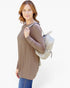 A woman wearing a brown long-sleeve tunic top and blue jeans, carrying a woven light beige backpack, photographed against a plain white background.