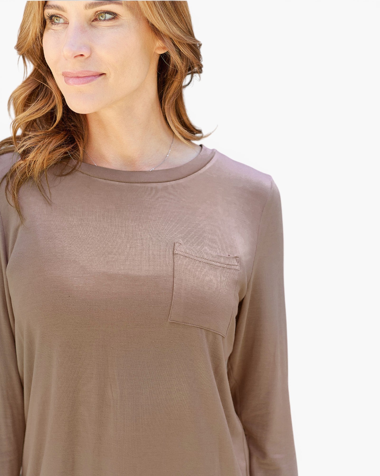 A woman wearing a long-sleeve crewneck top in a muted taupe-brown color, featuring a chest pocket, shown against a plain white background.