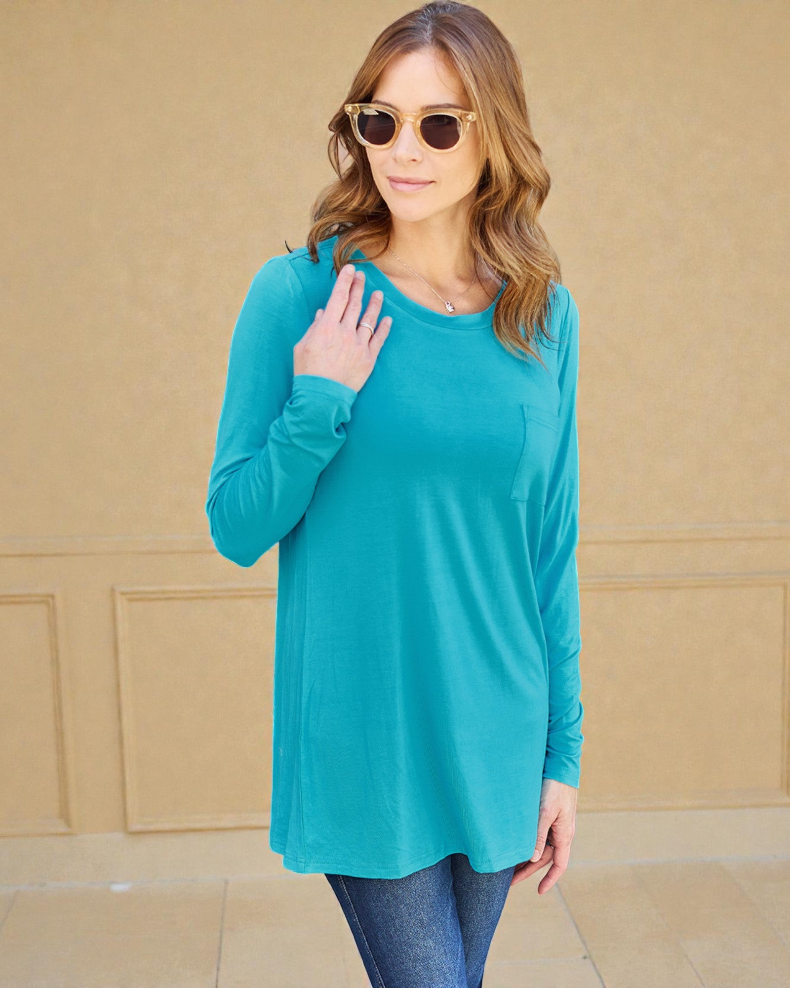 Woman wearing a turquoise long-sleeve top against a beige wall.