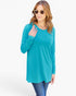 A woman modeling a bright turquoise long-sleeve tunic top with blue jeans against a plain white studio background.