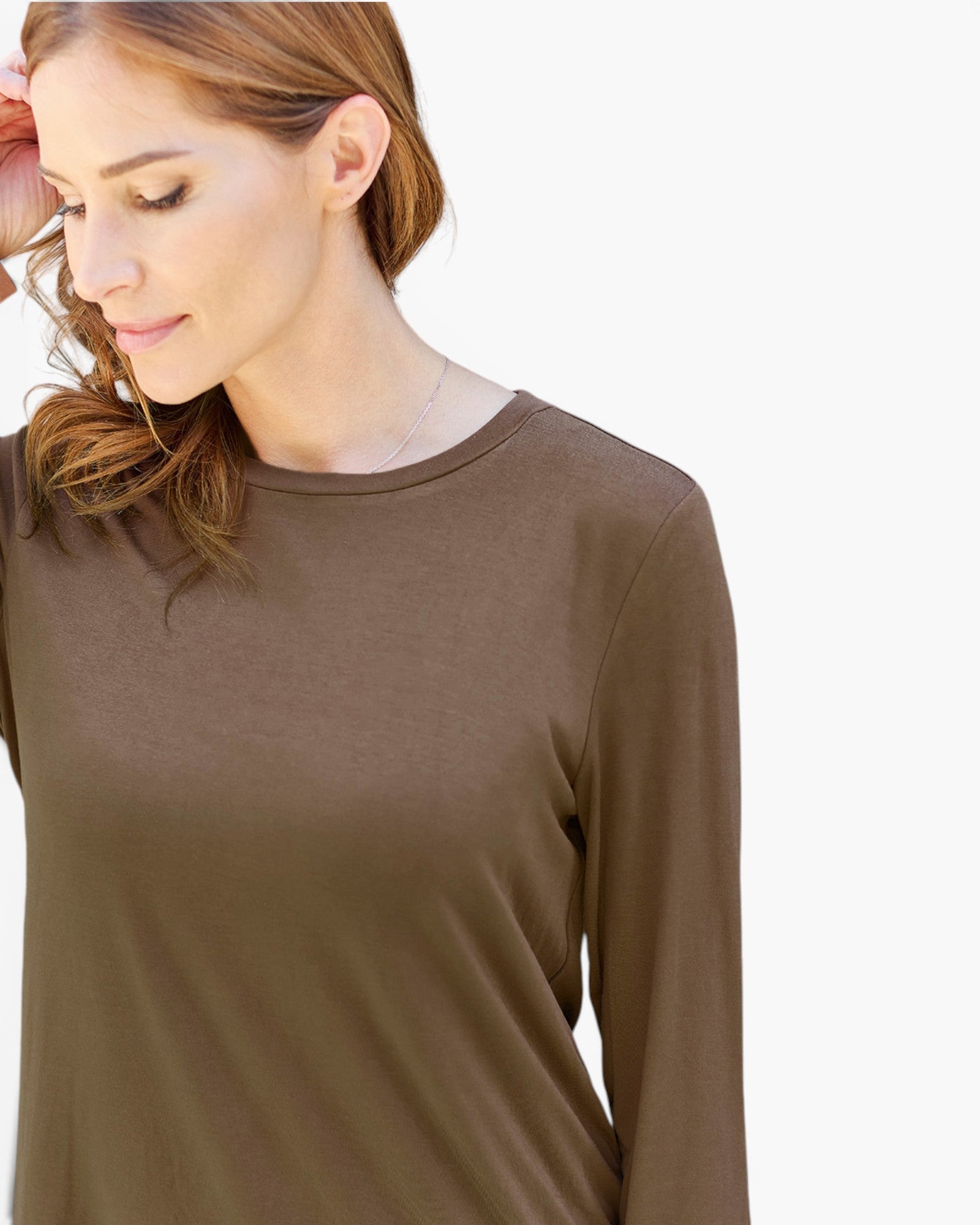 A woman wearing a plain brown long-sleeve crewneck top, shown from the chest up against a light gray background.