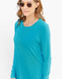 A woman wearing a bright turquoise long-sleeve crewneck top, gold-framed sunglasses, and a delicate necklace, shown against a plain white background.