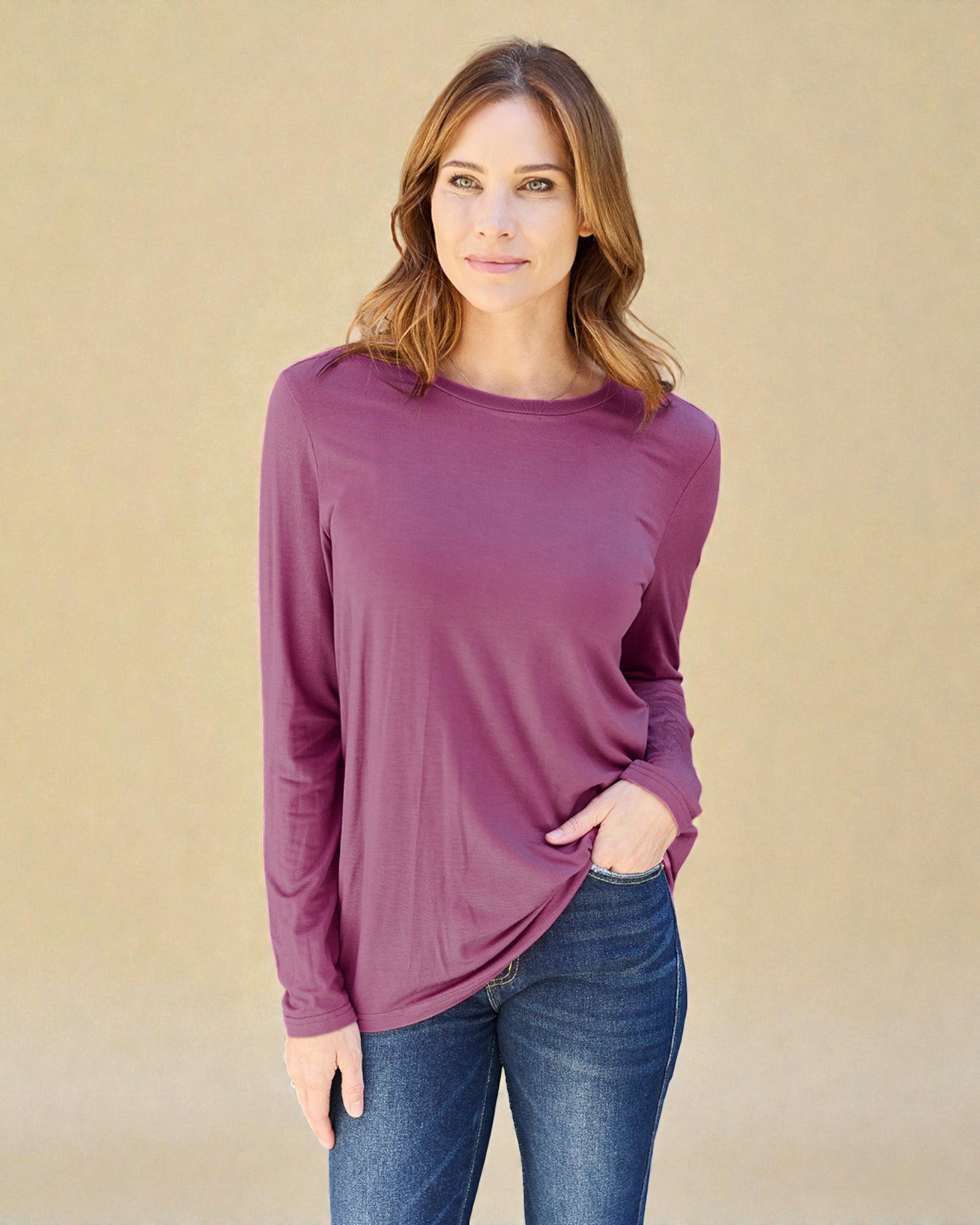 Woman wearing a purple long-sleeve top and blue jeans against a beige background