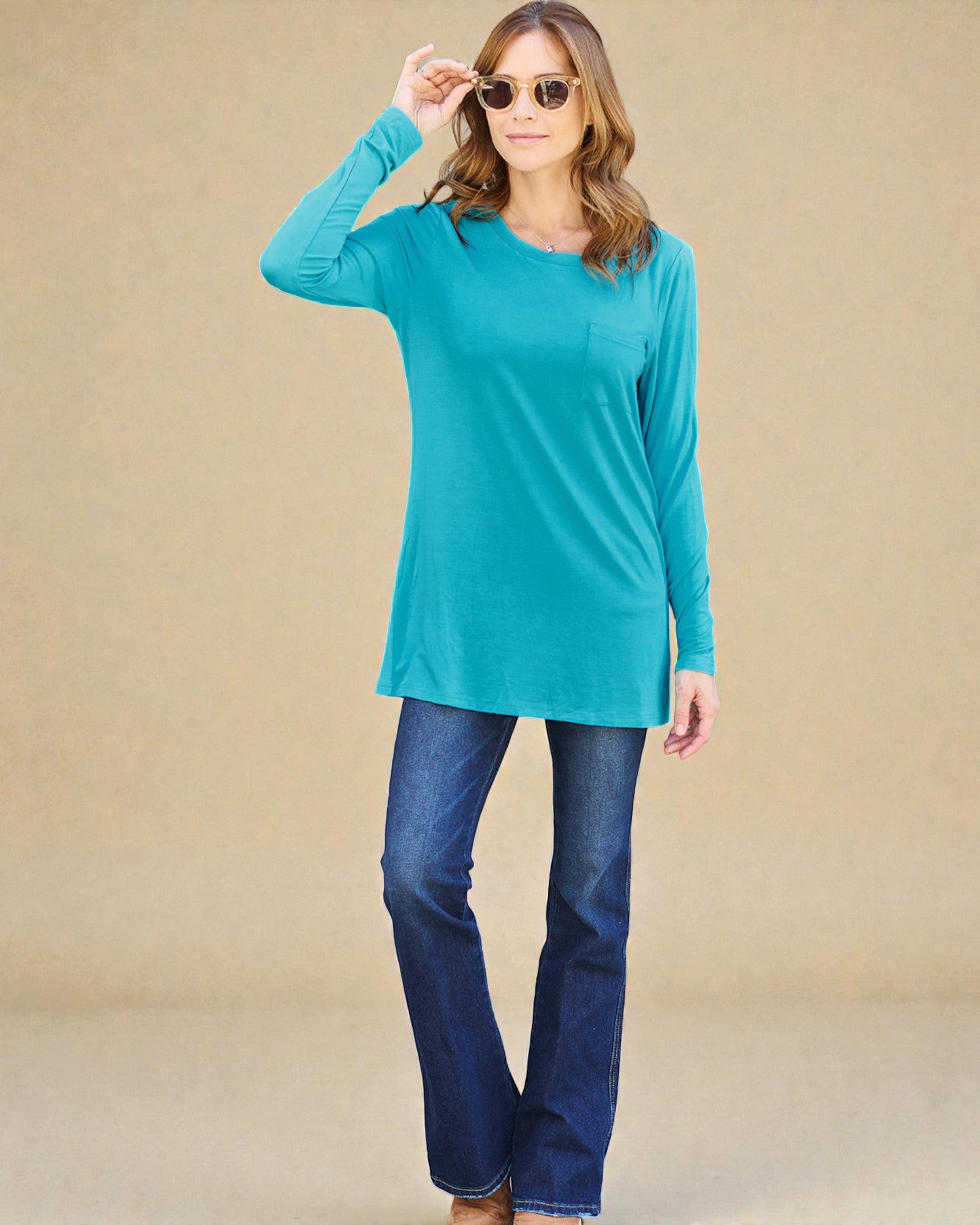 Woman wearing a turquoise long-sleeve top and blue jeans against a beige background