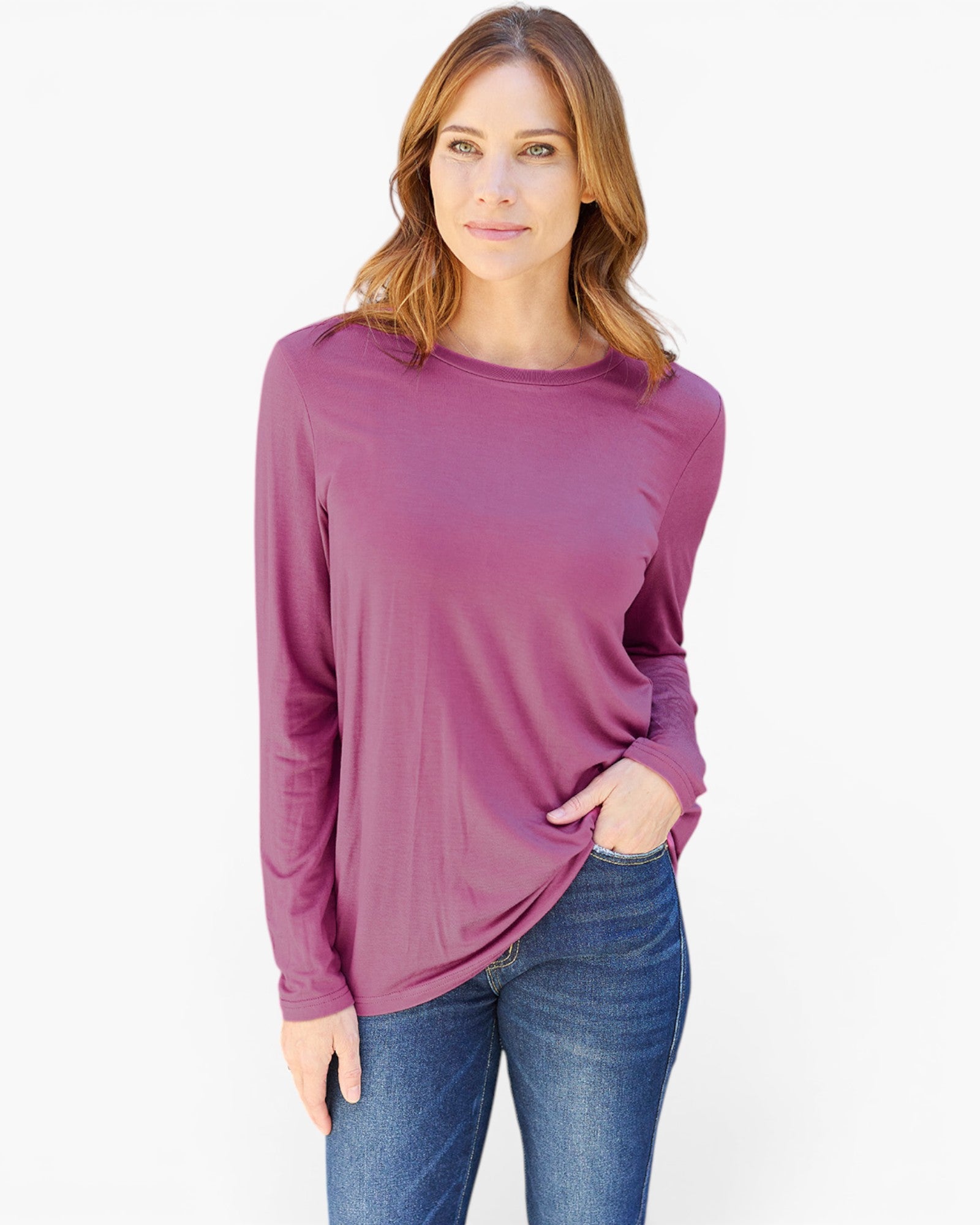 A woman wearing a long-sleeve crewneck top in a dusty mauve-purple color, paired with blue jeans, against a plain white studio background.
