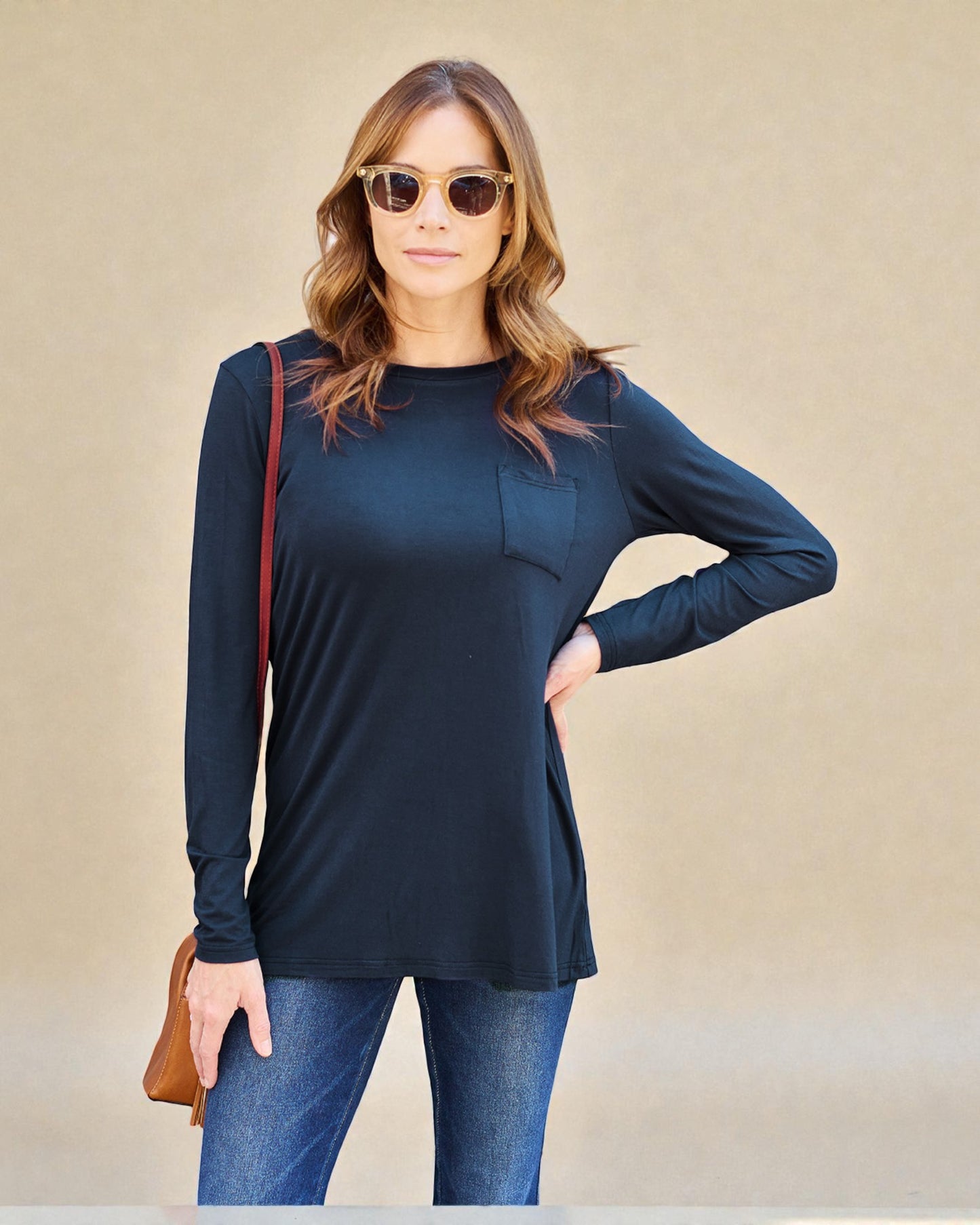 Woman wearing a navy long-sleeve top and blue jeans, standing against a beige background.