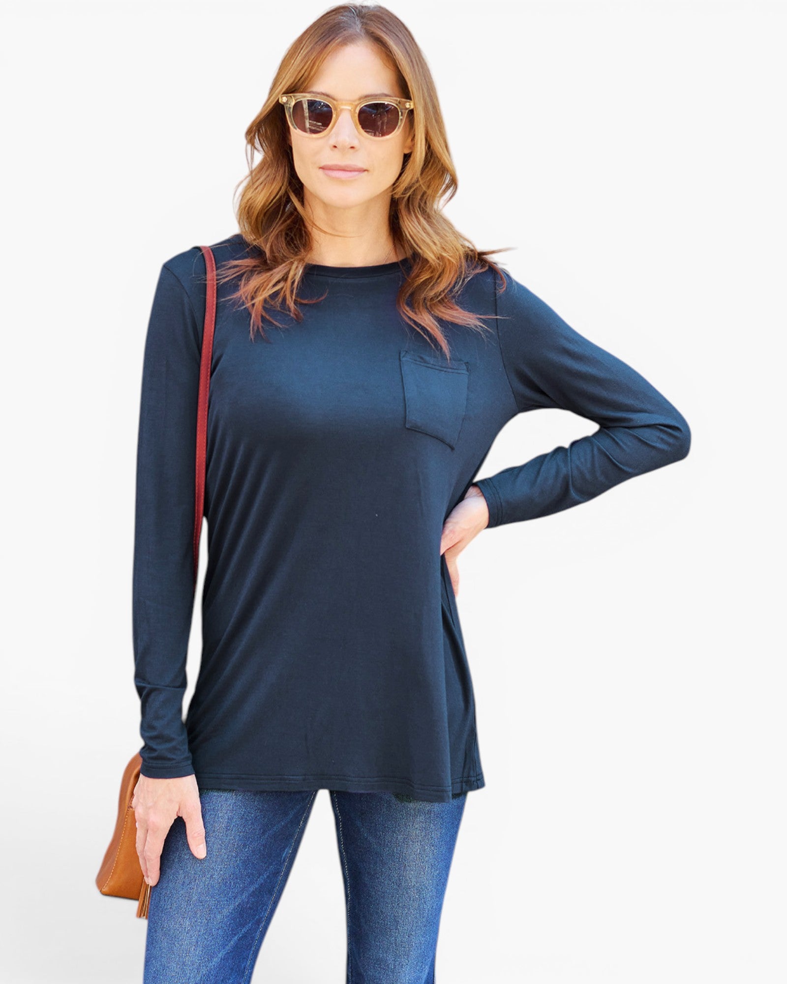 A woman modeling a dark navy blue long-sleeve tunic top with a chest pocket, paired with blue jeans and sunglasses, against a plain white background.
