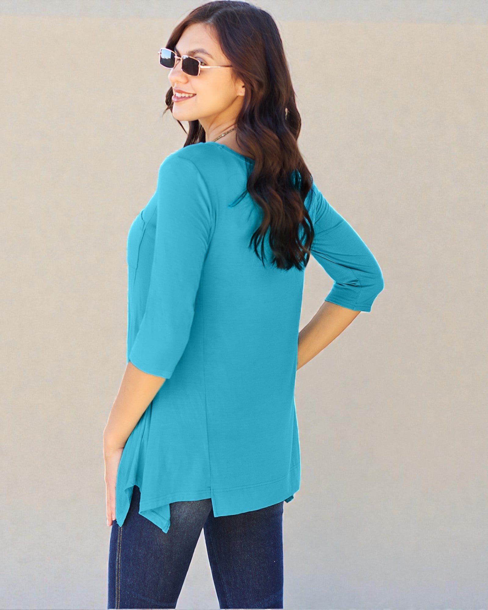 Woman wearing a turquoise top and sunglasses against a beige wall