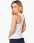 A woman wearing a white sleeveless tank top and dark blue jeans, photographed from the back against a clean white studio background.