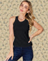 Woman wearing a black sleeveless top and blue jeans against a patterned wall.