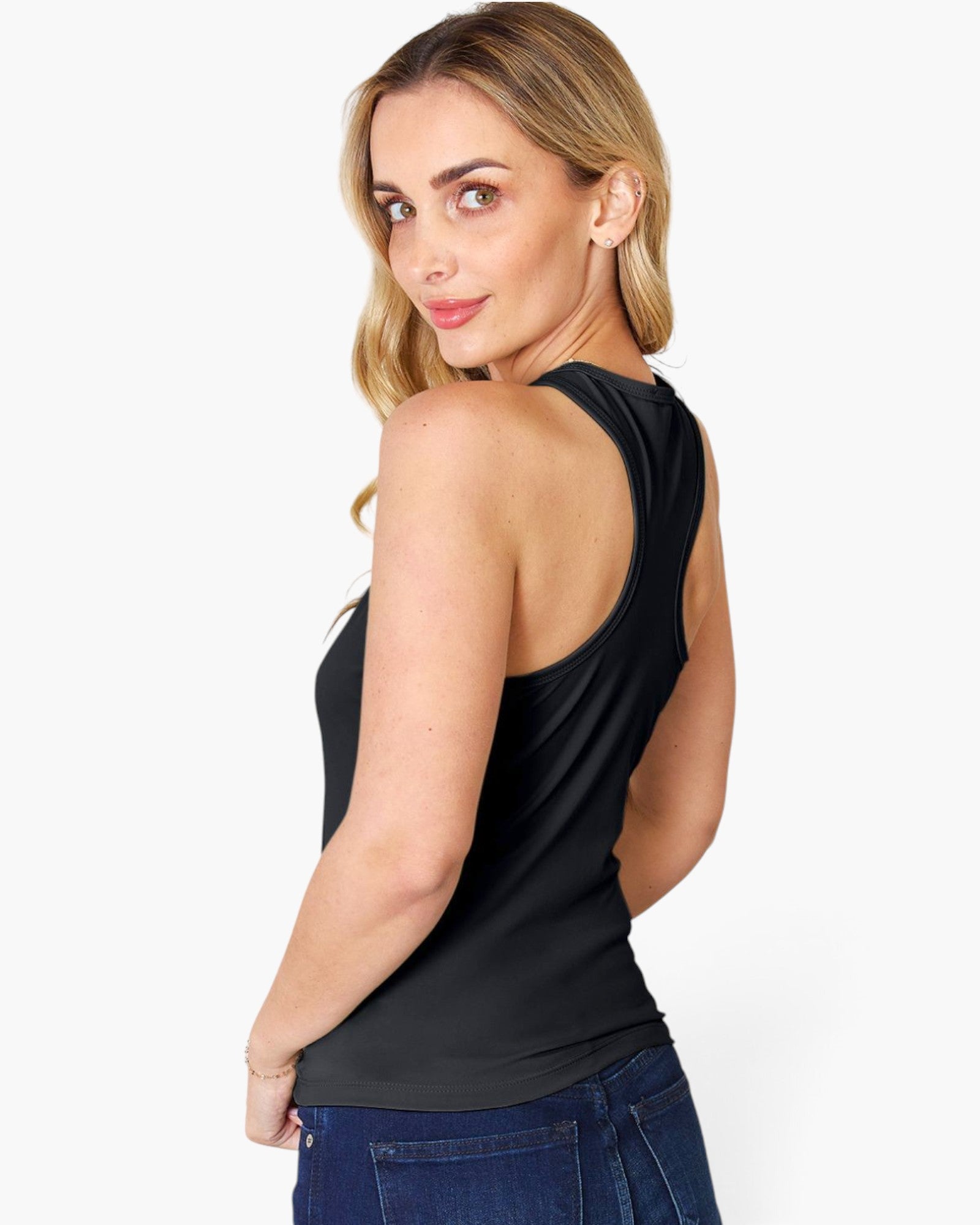 A woman wearing a black sleeveless tank top and blue jeans, shown from a side-back angle against a plain light gray studio background.