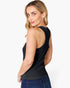 A woman wearing a black sleeveless tank top and blue jeans, shown from a side-back angle against a plain light gray studio background.