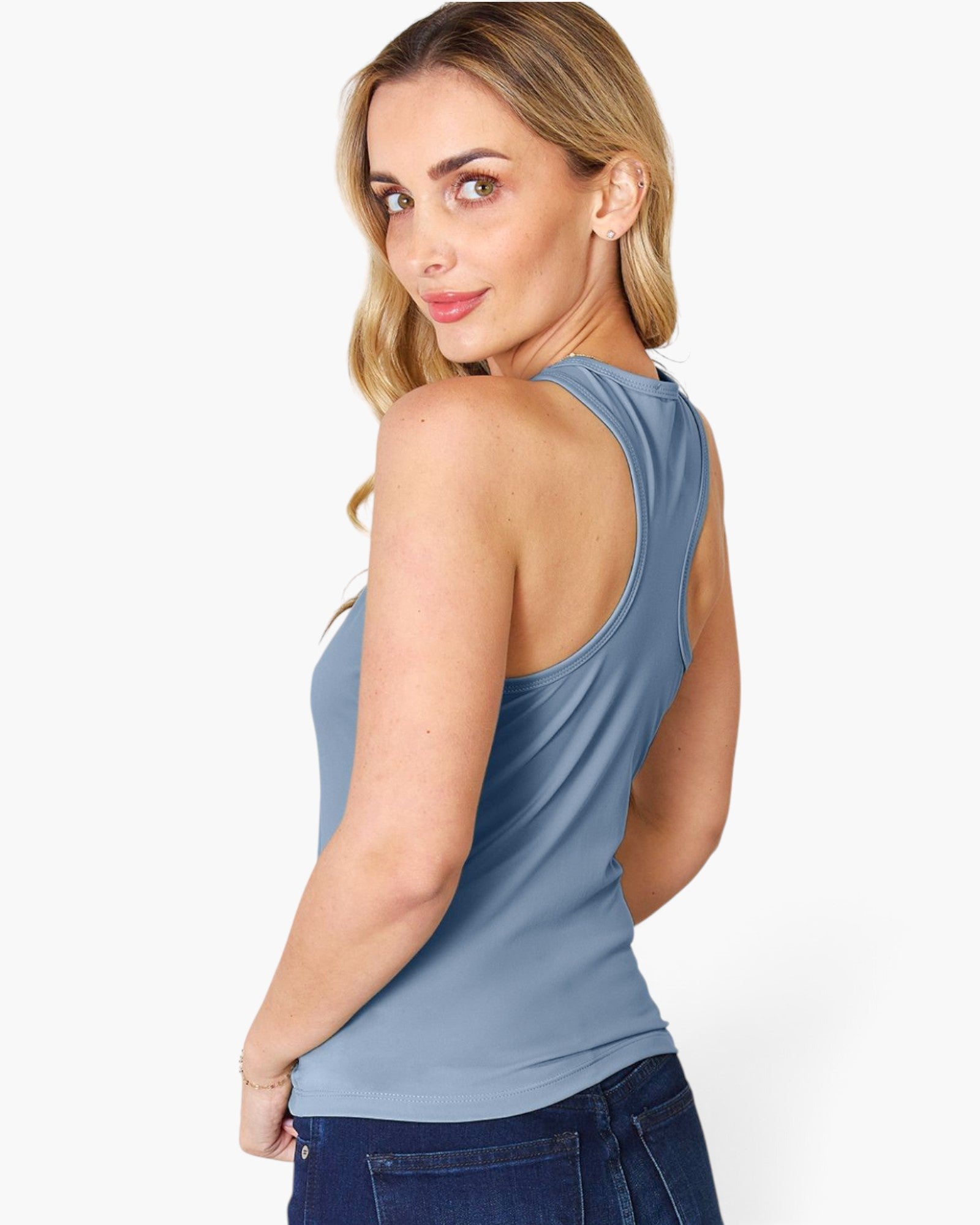 A woman wearing a sleeveless racerback tank top in dusty blue, shown from a three-quarter back view against a plain white studio background.