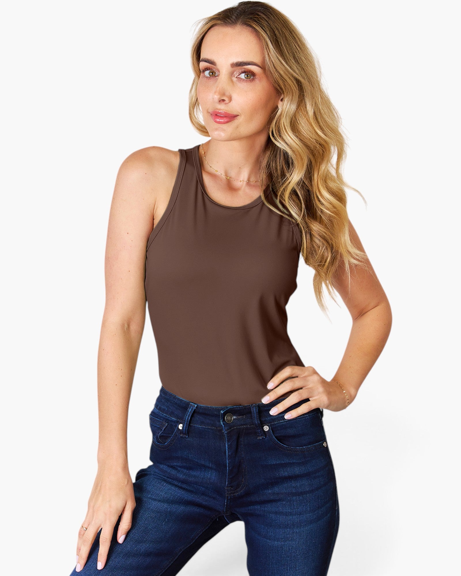 A woman modeling a sleeveless brown tank top paired with dark blue jeans, posed against a clean white studio background.