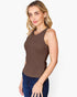 A woman modeling a sleeveless brown scoop-neck tank top paired with dark blue jeans, photographed against a clean white studio background.