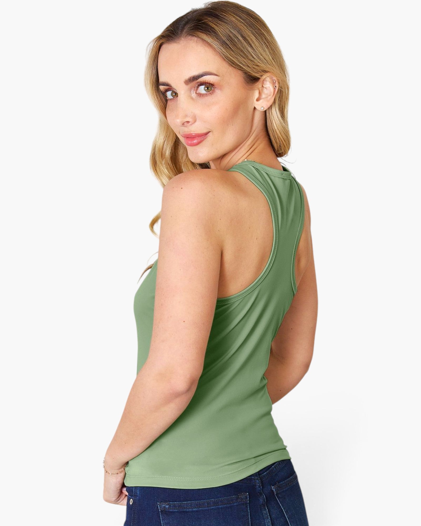 A woman wearing a sage green racerback tank top and blue jeans, shown from a three-quarter back view against a plain white studio background.