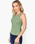 A woman modeling a sleeveless scoop-neck tank top in sage green, paired with dark blue jeans, against a plain light gray background.