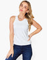 A woman modeling a white sleeveless tank top paired with dark blue jeans, posed against a clean white studio background.