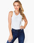 A woman modeling a white sleeveless scoop-neck tank top paired with dark blue jeans, set against a plain white studio background.