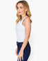 A woman wearing a white sleeveless tank top and dark blue jeans, shown from a side profile against a plain white studio background.