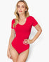A woman modeling a bright red short-sleeve scoop-neck bodysuit against a light gray studio background.