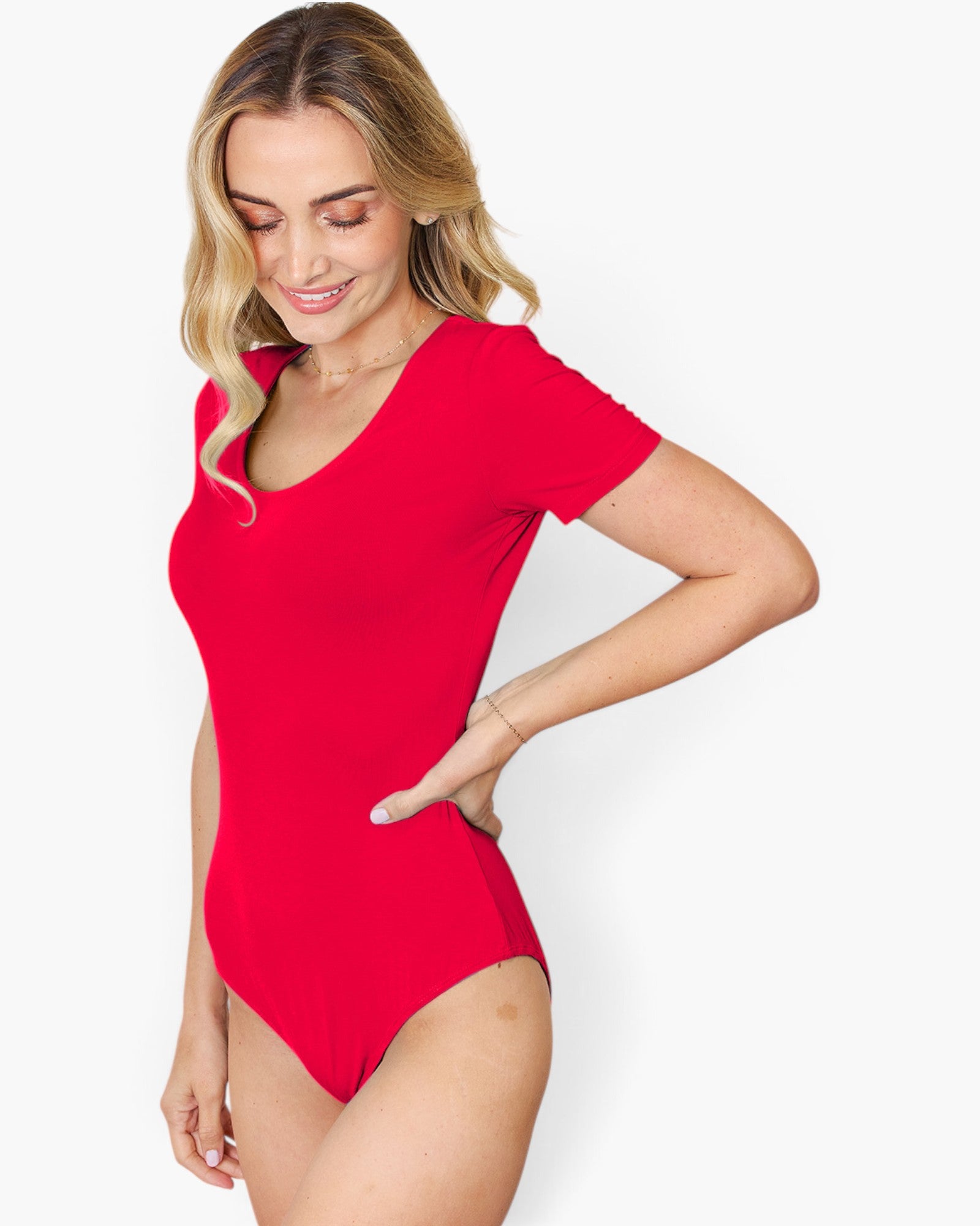 A woman modeling a bright red short-sleeve bodysuit or one-piece swimsuit against a clean light gray studio background.
