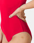 A close-up of a model wearing a bright red one-piece swimsuit, showing the side hip and hand resting on the hip against a light gray background.
