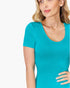 A woman wearing a bright turquoise short-sleeve scoop-neck top, shown from the chest up against a plain white background.