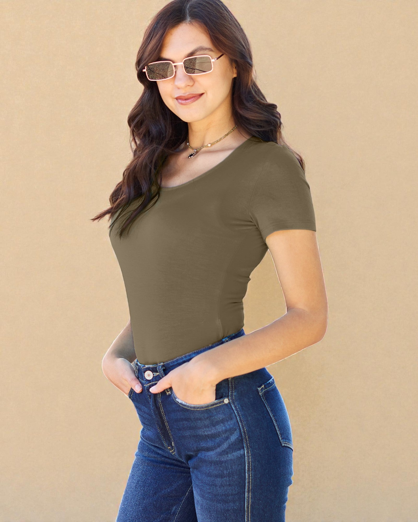 Woman wearing an olive green top and blue jeans against a beige background