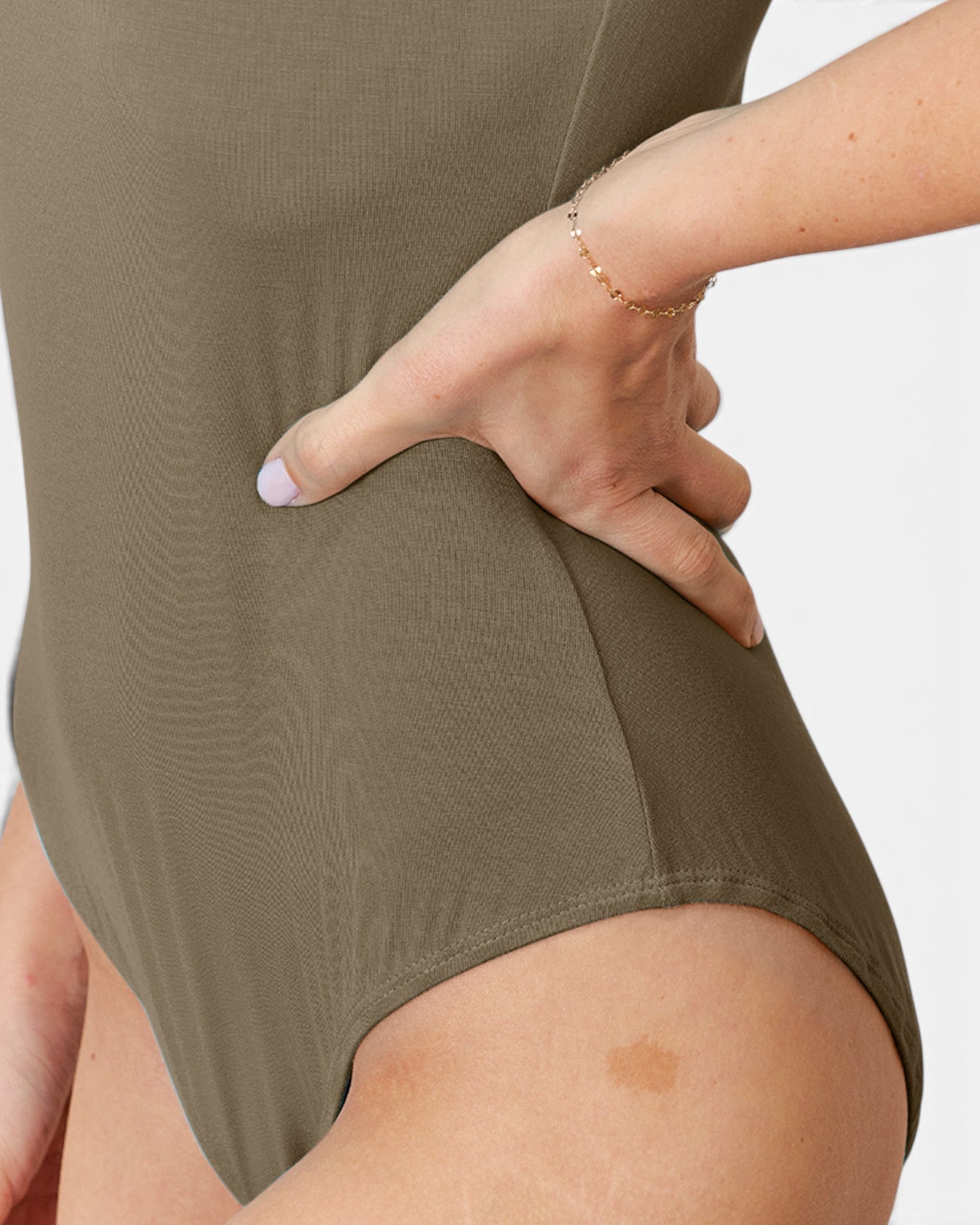 Close-up of a person wearing a ribbed olive green bodysuit, with one hand resting on the hip area against a plain light background.