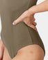Close-up of a person wearing a ribbed olive green bodysuit, with one hand resting on the hip area against a plain light background.