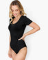 A woman modeling a black short-sleeve bodysuit with a scoop neckline against a plain light gray studio background.