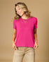 Woman wearing a bright pink top and beige pants against a beige background