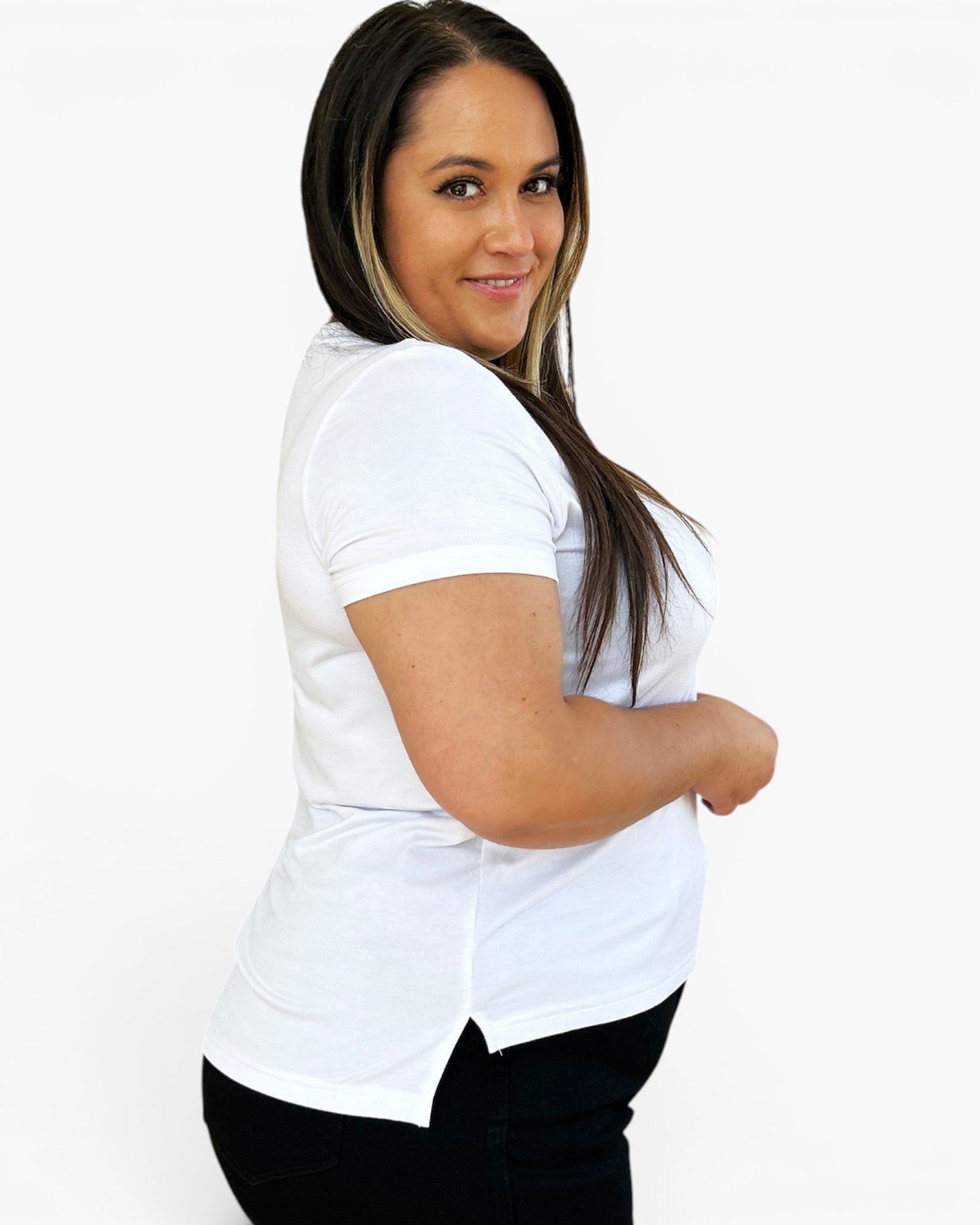 A woman with long dark hair is wearing a white short-sleeve crewneck t-shirt and black pants, posing against a solid white studio background.