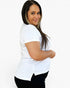 A woman with long dark hair is wearing a white short-sleeve crewneck t-shirt and black pants, posing against a solid white studio background.