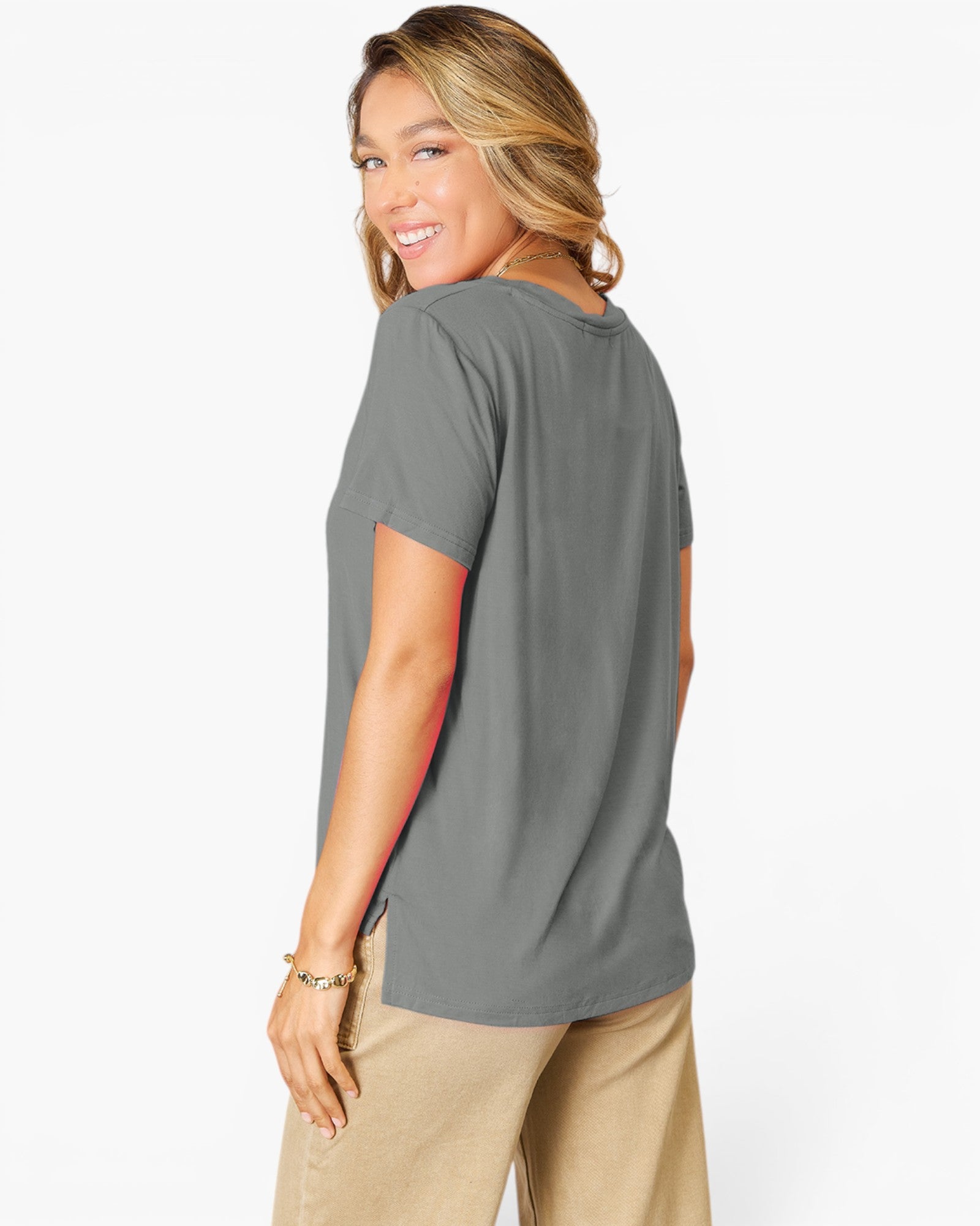 A woman wearing a short-sleeve gray t-shirt and beige pants, shown from a side-back angle against a plain white studio background.
