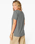 A woman wearing a short-sleeve gray t-shirt and beige pants, shown from a side-back angle against a plain white studio background.