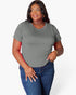 A woman modeling a short-sleeve crewneck t-shirt in a solid gray color, paired with blue jeans, against a plain light gray background.