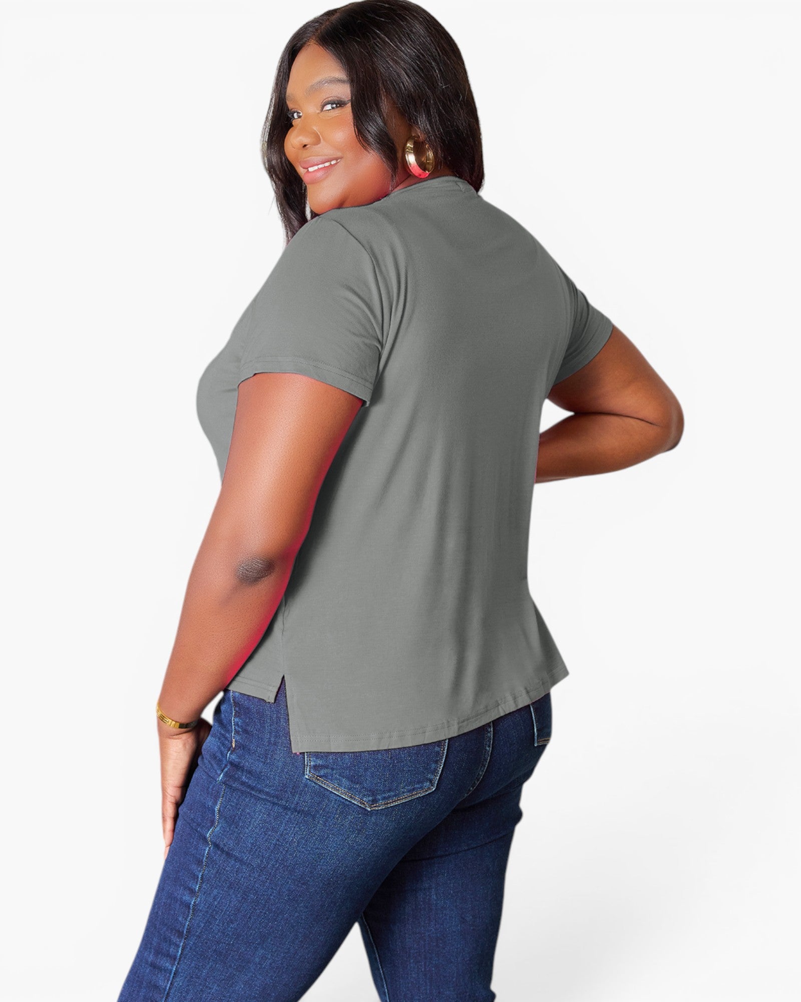 A woman wearing a short-sleeve gray t-shirt and blue jeans, shown from a back-three-quarter angle against a light gray studio background.